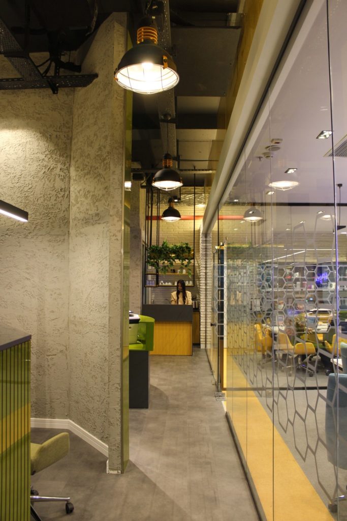 Modern office interior with industrial lighting and glass partitions, featuring a reception area with a green and yellow color scheme.